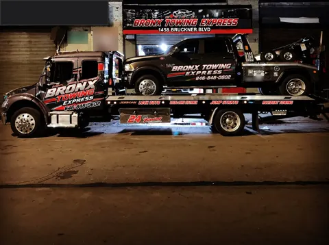 Bronx Towing Express flatbed carrying a pickup outside 1458 Bruckner Blvd at night